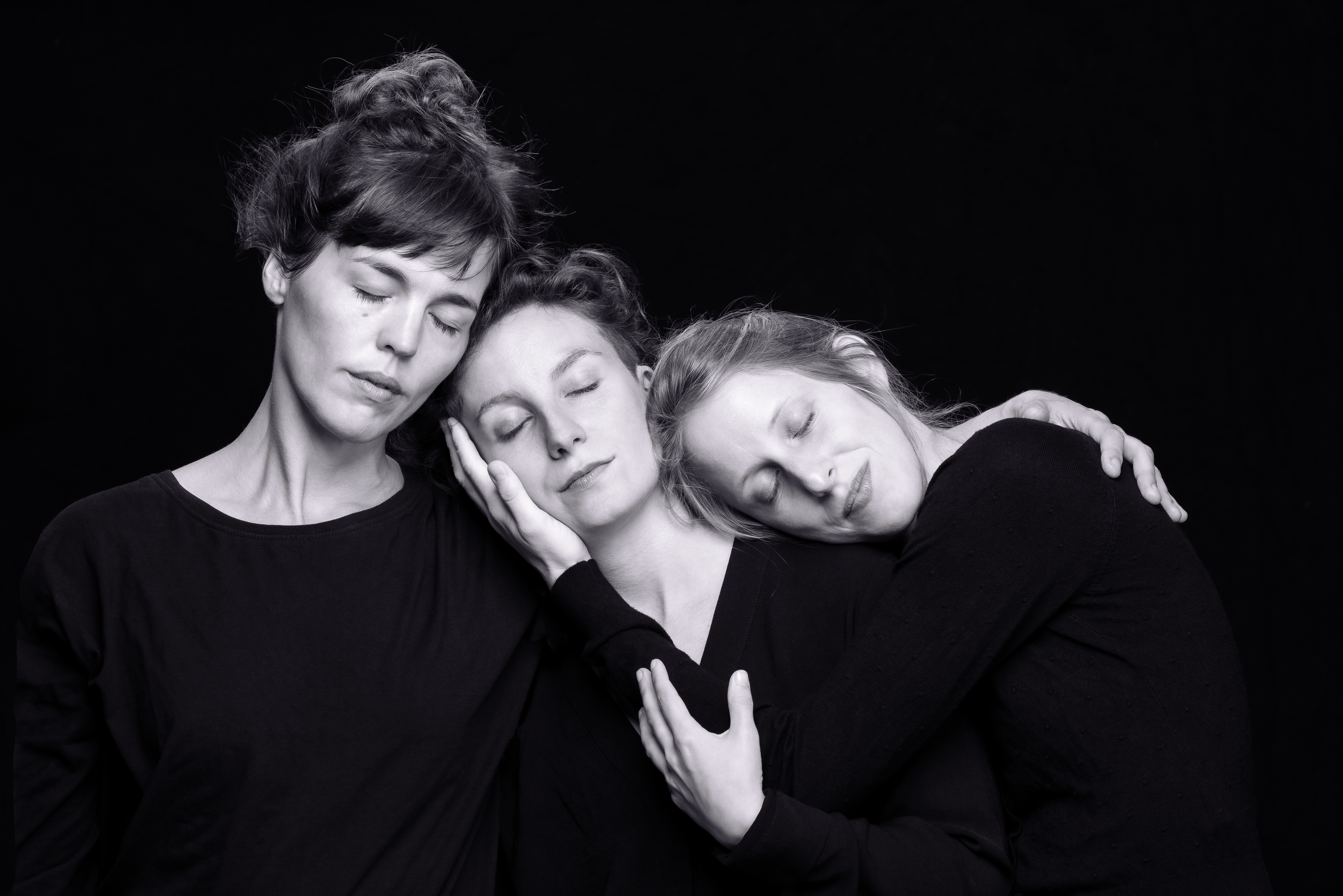 3 Frauen vor schwarzem Hintergrund, aneinander gelehnt, die Augen sind geschlossen